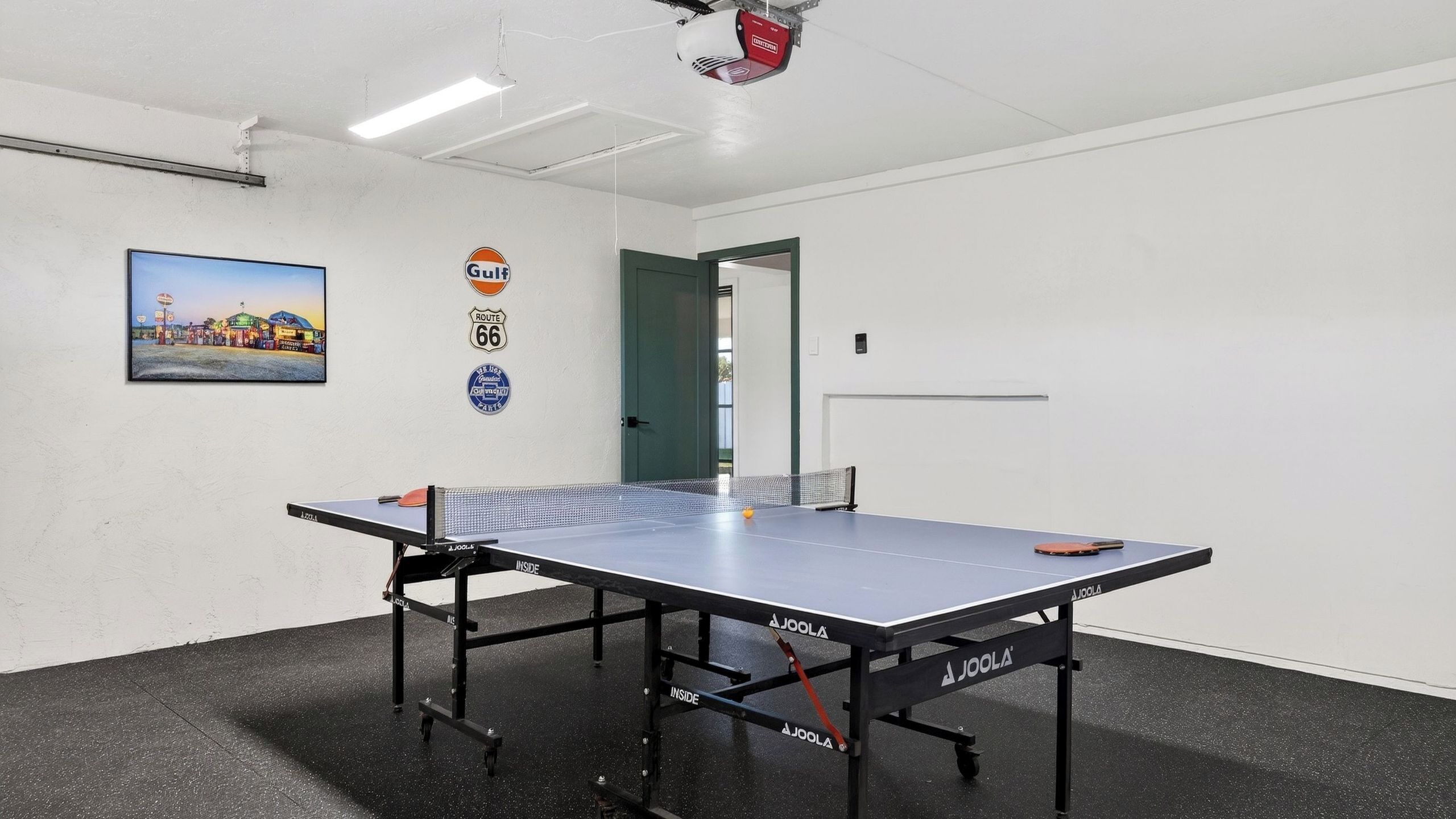 Une table de ping-pong dans une pièce avec un mur blanc, un tableau et une porte.