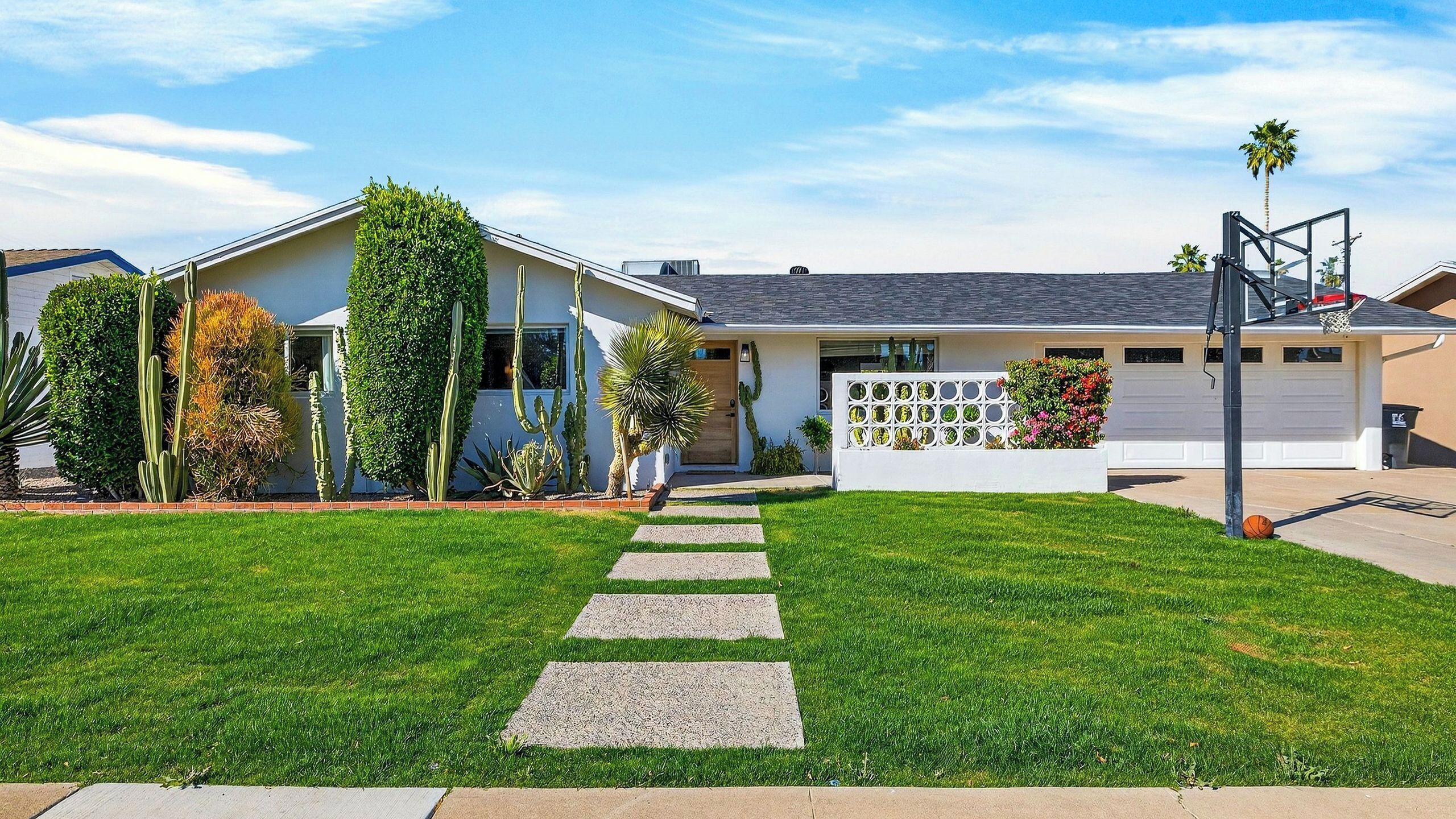 A residential house with a well-maintained lawn, a driveway leading to the garage, and a basketball hoop.