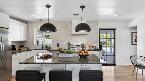 Una cocina moderna con una isla central, lámparas colgantes negras y un refrigerador de acero inoxidable.