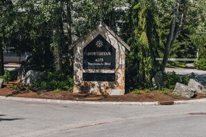 A stone sign with the text "NORTHSTAR 4355 Northlands Blvd" surrounded by greenery and trees. - Stoney Creek Northstar 105 (Whistler)