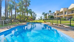 A swimming pool with a curved design, surrounded by palm trees and a fenced area. - Elsinor 4 Located a short stroll from Lake Mulwala and the popular local clubs. (Mulwala)