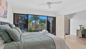 A bedroom with a bed, a ceiling fan, a large window, and a view of palm trees. - Elsinor 4 Located a short stroll from Lake Mulwala and the popular local clubs. (Mulwala)