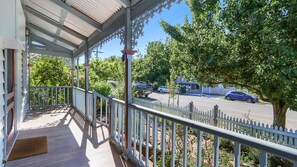 A covered porch with a railing, a wooden deck, and a view of a parking lot with cars and trees. - Audrey's Of Beechworth NEW Listing (Beechworth)