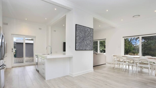A modern kitchen with a central island, a dining area with white chairs, and a large window providing natural light. - Clare Valley vineyard - Pool and walk to wineries - perfect for groups (Sevenhill)