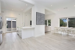A modern kitchen with a central island, a dining area with white chairs, and a large window providing natural light. - Clare Valley vineyard - Pool and walk to wineries - perfect for groups (Sevenhill)