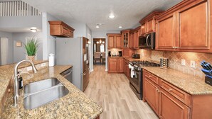 Una cocina con encimeras de granito, electrodomésticos de acero inoxidable, armarios de madera y un salpicadero con diseño en espiga.