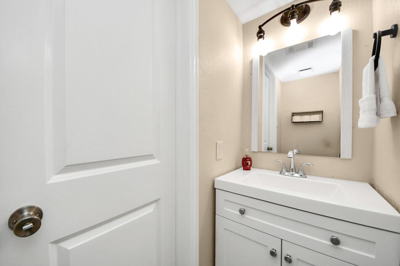A bathroom with a white door, a sink with a mirror, and a towel rack.