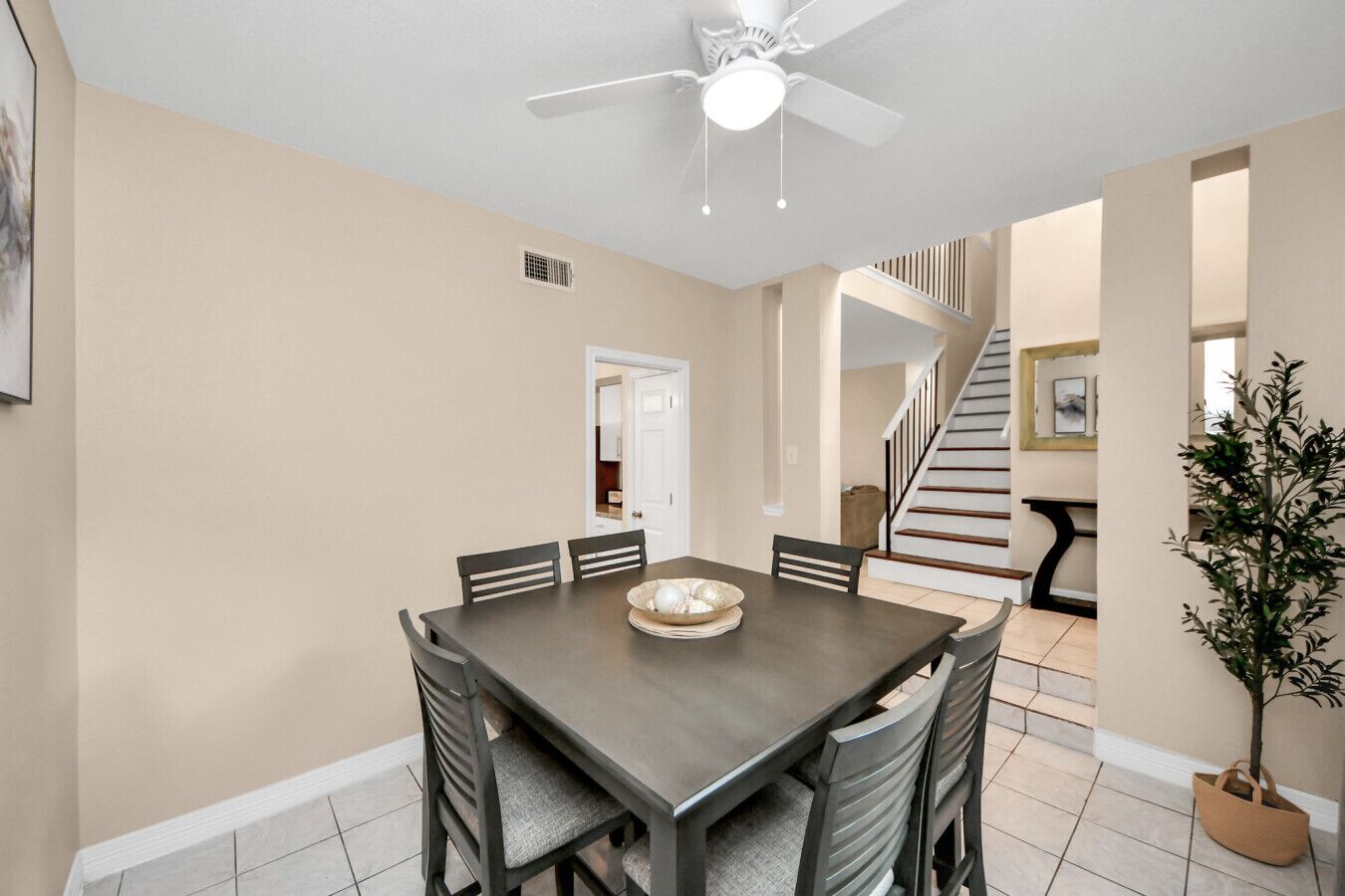 A dining area with a dark wooden table, six chairs, a ceiling fan, and a potted plant.