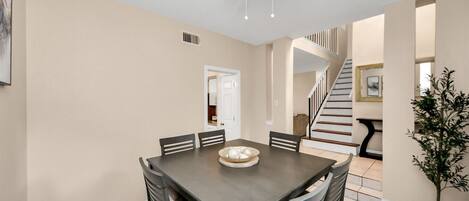 A dining area with a dark wooden table, six chairs, a ceiling fan, and a potted plant.