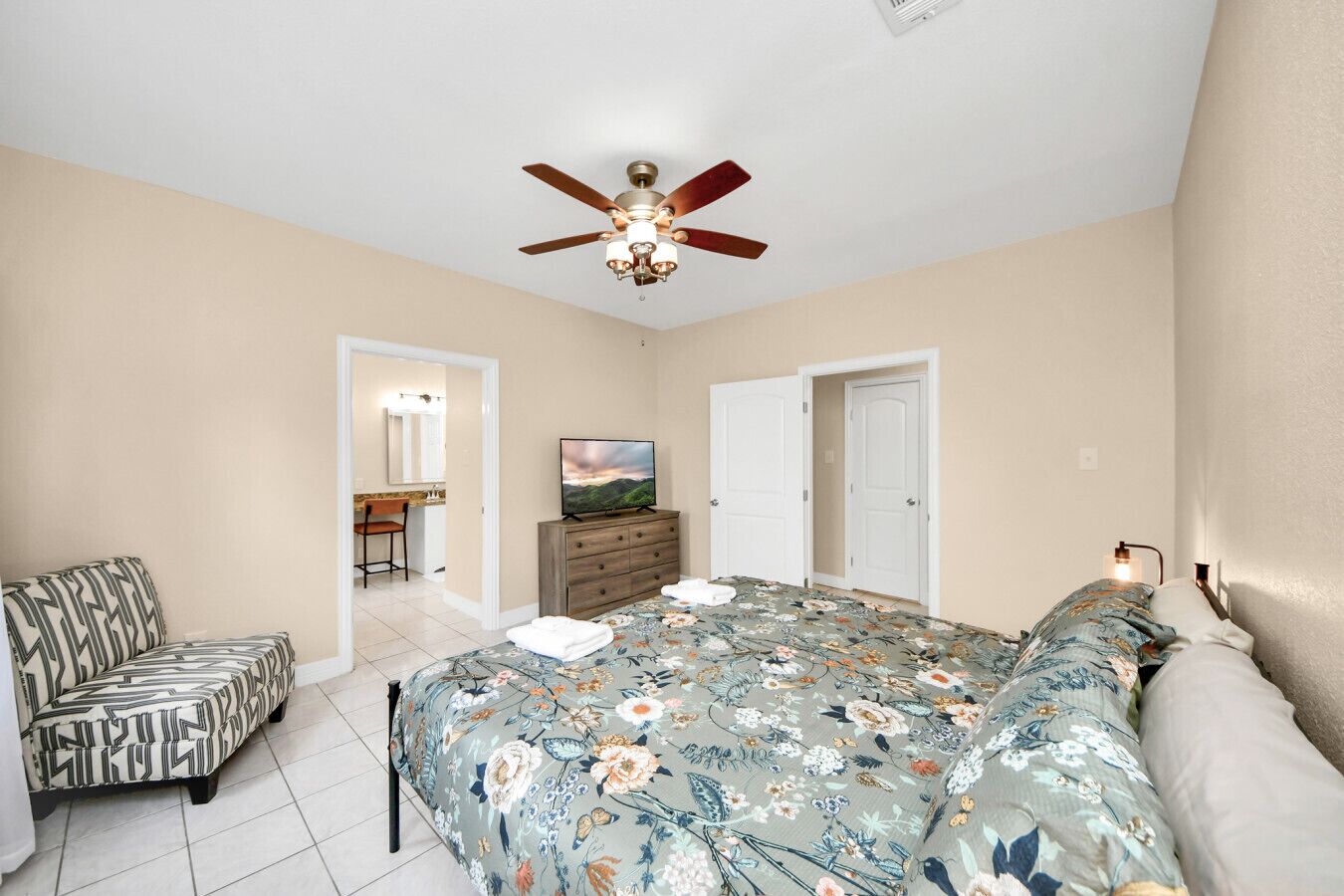 A bedroom with a bed, a ceiling fan, a dresser, and a TV.