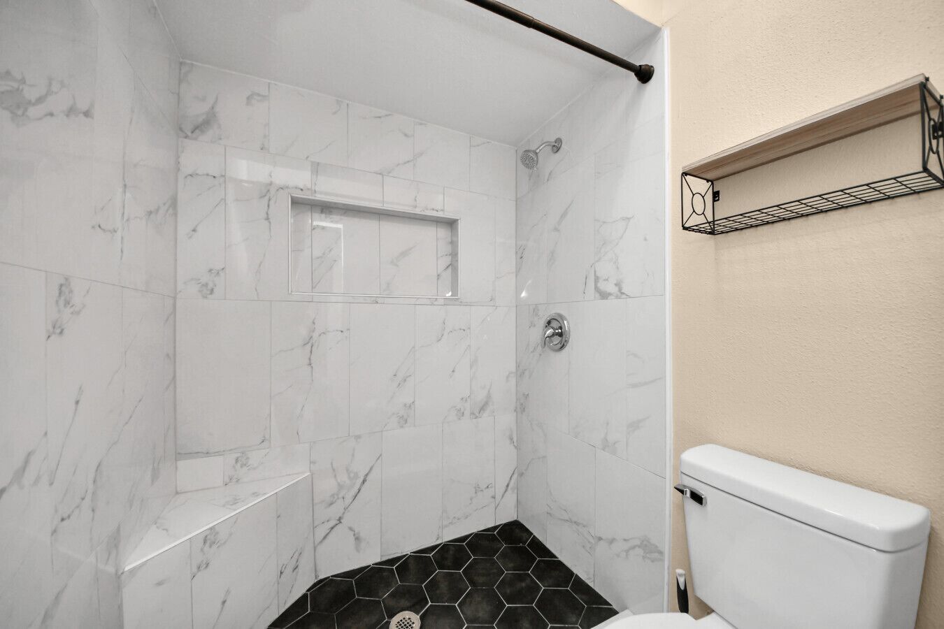 A bathroom with a shower, a toilet, and a shelf.