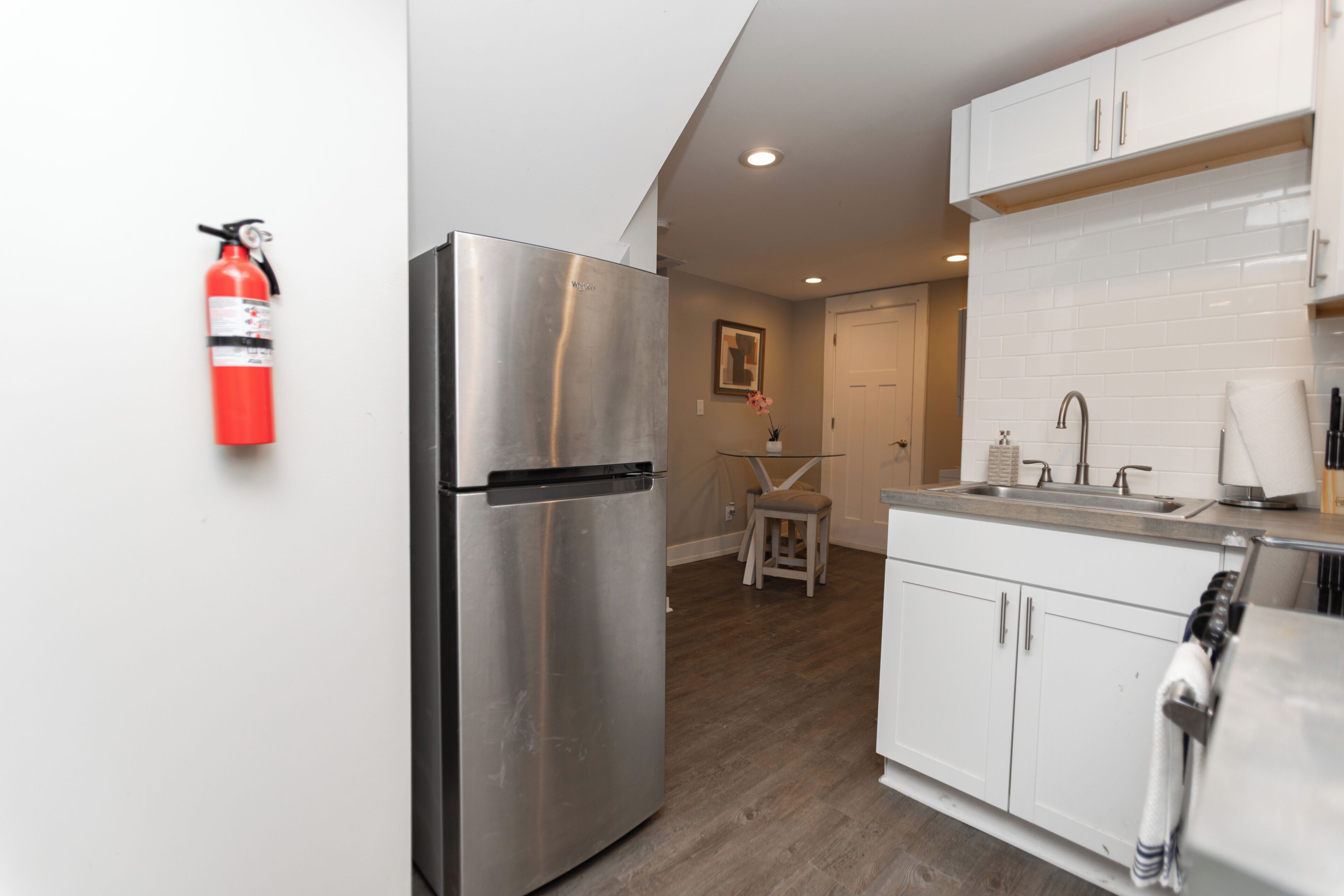 A modern kitchen with stainless steel appliances, white cabinets, and a small dining area with a table and chairs.