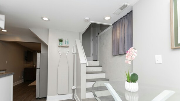 Una cocina moderna con refrigerador, un comedor con mesa de vidrio y una escalera que sube a otro nivel.