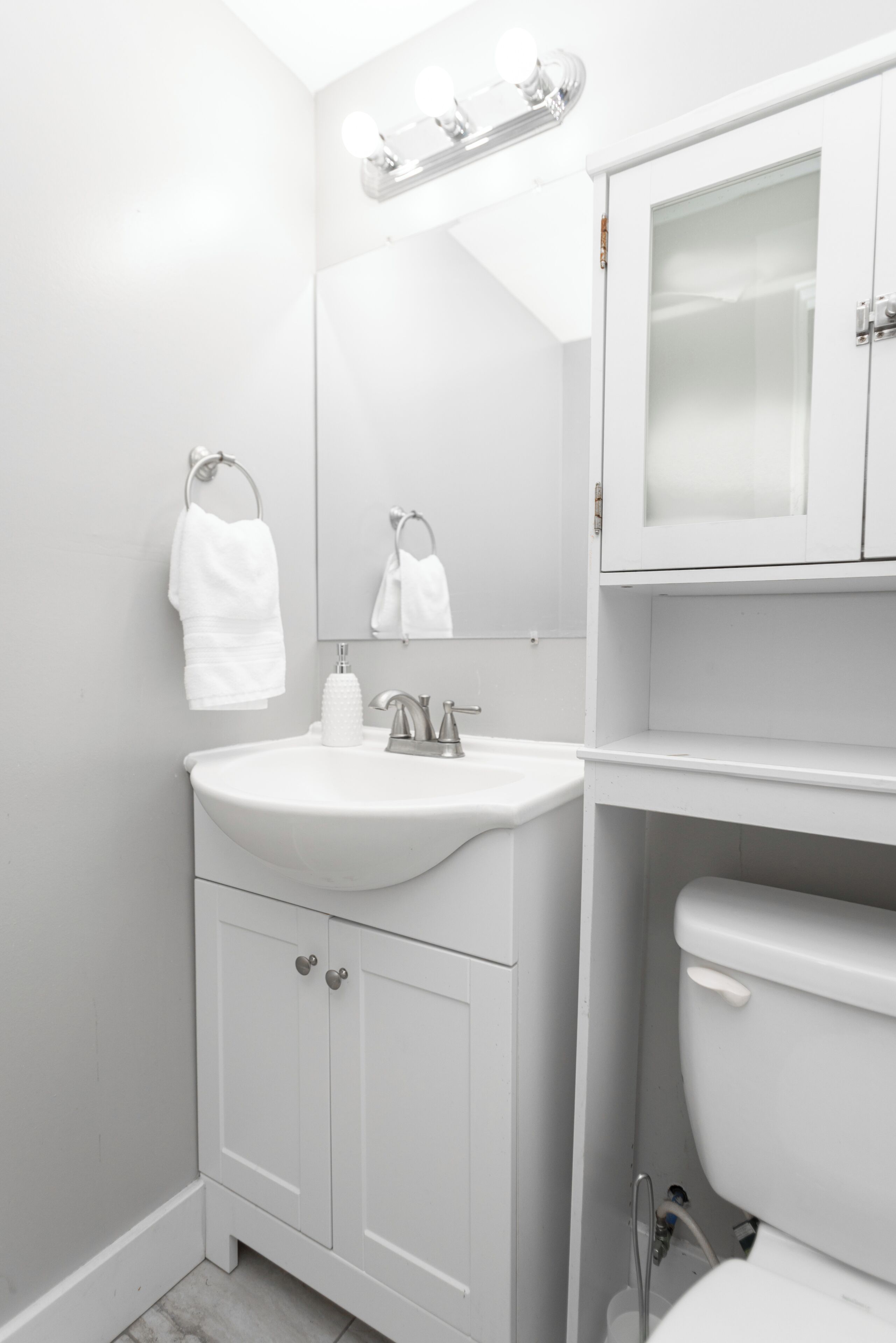 Ein modernes Badezimmer mit Waschbecken, Spiegel und Schrank in Weiß sowie einer Toilette.