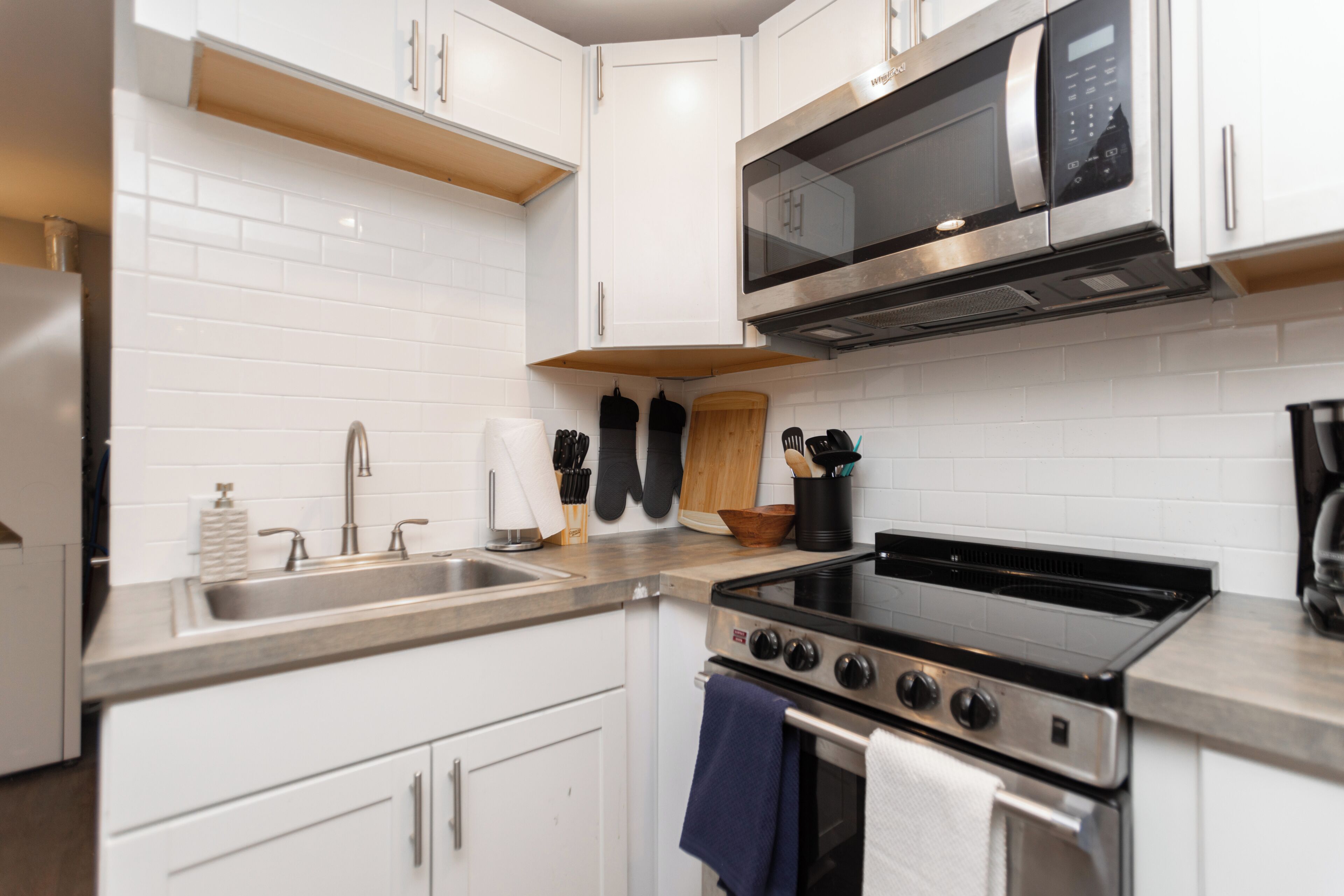 A modern kitchen with white cabinets, stainless steel appliances, and a wooden countertop.