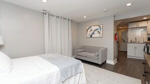 Una habitación de hotel moderna con cama, sofá gris, zona de cocina y extintor.