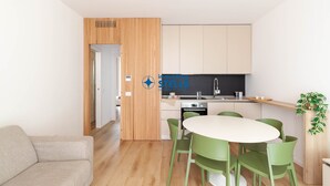Eine moderne Küche mit Einbauofen, Spüle und Arbeitsplatte. Ein Essbereich mit rundem Tisch und grünen Stühlen ist ebenfalls vorhanden.