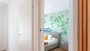 Ein Schlafzimmer mit einem Bett, einem Nachttisch, einer Wand mit grünem Blattmuster und einem Holzboden.