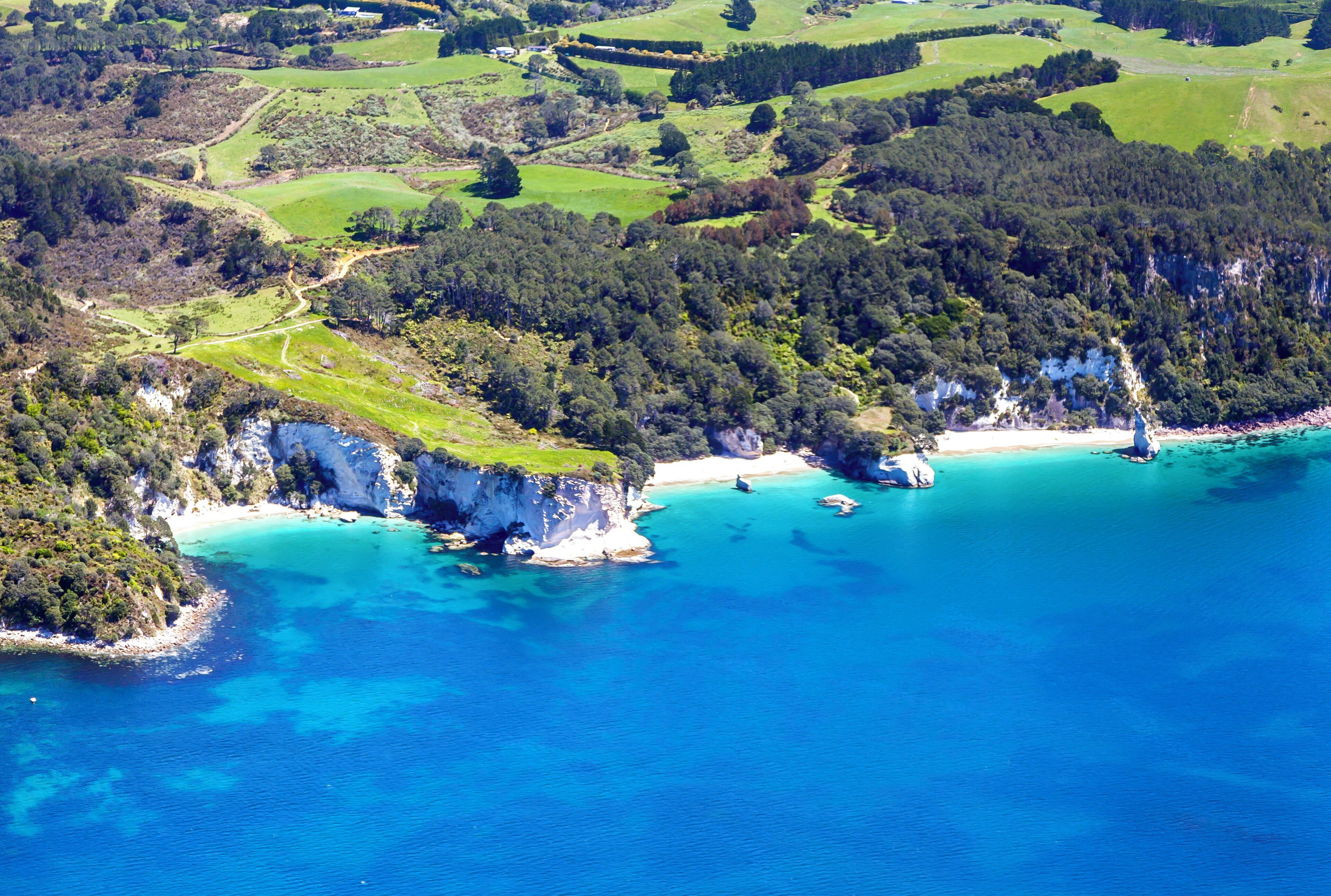 An aerial view of a coastal area with cliffs, clear blue waters, and green fields.