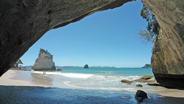 A beach scene with a large rock formation in the foreground and a clear blue sky. - Sweeping panoramic views of Hahei beach and offshore islands (Hahei)