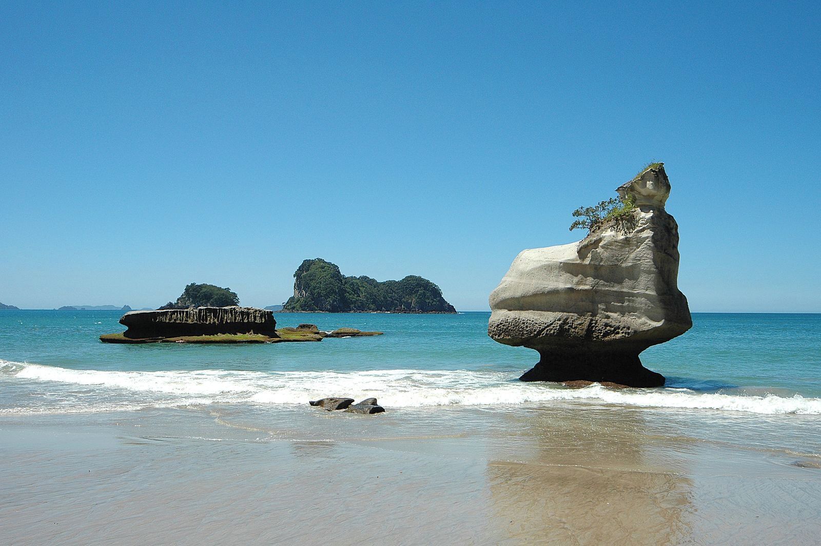 Une plage avec une grande formation rocheuse et un bateau sur l’eau.