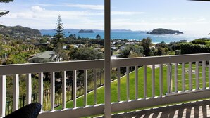A balcony with a view of a coastal landscape, including hills, a body of water, and distant islands. - Sweeping panoramic views of Hahei beach and offshore islands (Hahei)