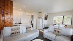 A modern living room with two sofas, a small table, and a kitchen area in the background. - Sweeping panoramic views of Hahei beach and offshore islands (Hahei)