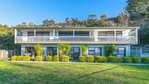 A two-story house with a balcony, a front porch, and a well-maintained lawn. - Sweeping panoramic views of Hahei beach and offshore islands (Hahei)