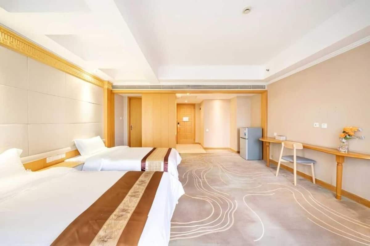 Une chambre d’hôtel avec deux lits, un bureau, une chaise et une petite table agrémentée de fleurs.