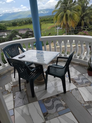 Une terrasse avec une table et des chaises, un pilier bleu et une vue sur un paysage verdoyant avec des montagnes.