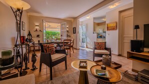 A spacious living area with a dining table, chairs, a sofa, a TV, and a kitchen visible through an open door. - GRIMAUD – BEAUTIFUL PROVENCAL VILLA IN THE HEART OF THE VILLAGE (GRIMAUD)