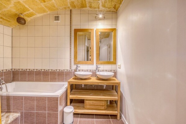 A bathroom with a bathtub, two sinks, wooden vanity, and a mirror.