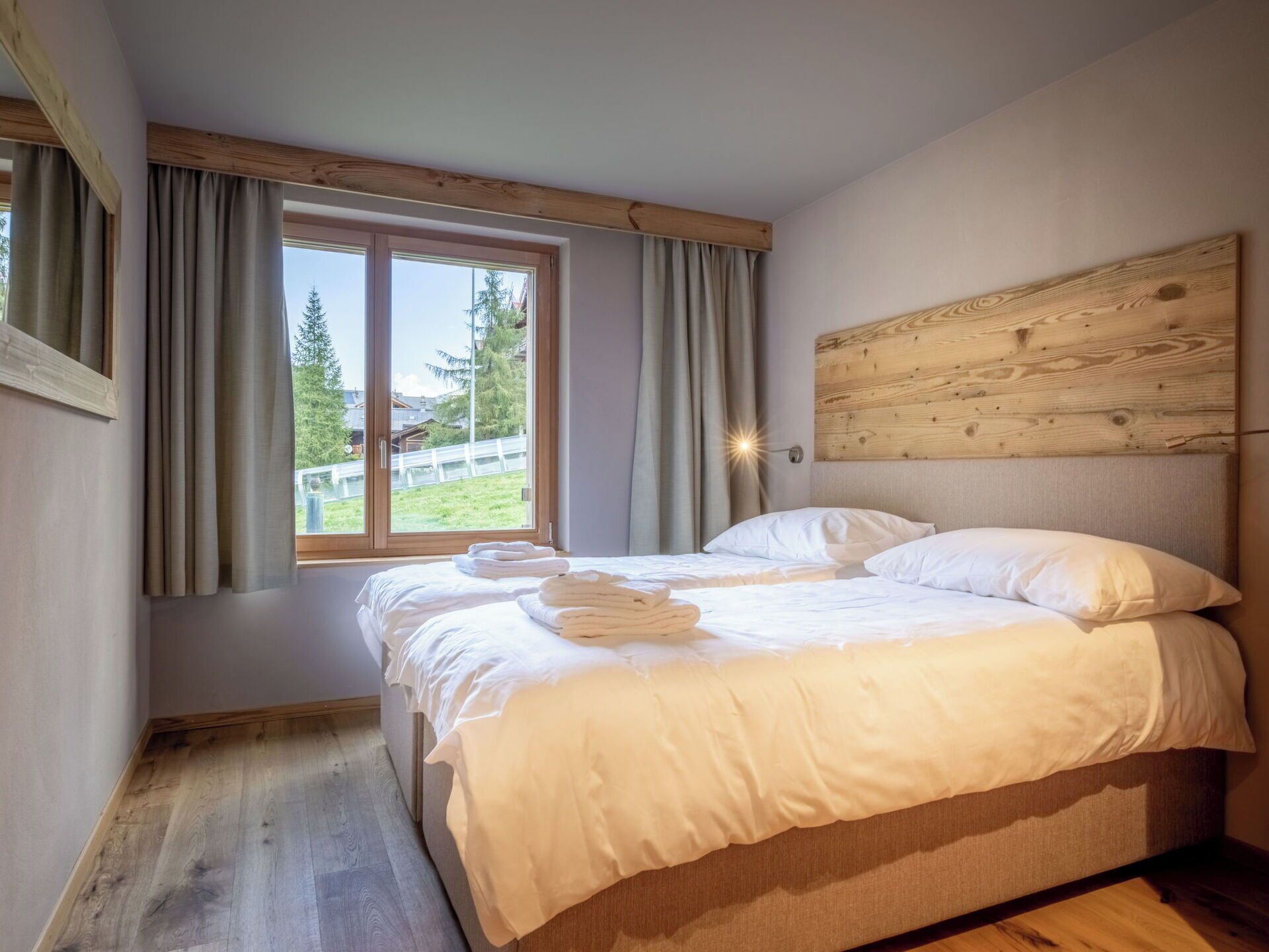 A bedroom with a large bed, wooden headboard, and a view of a green landscape through a window.