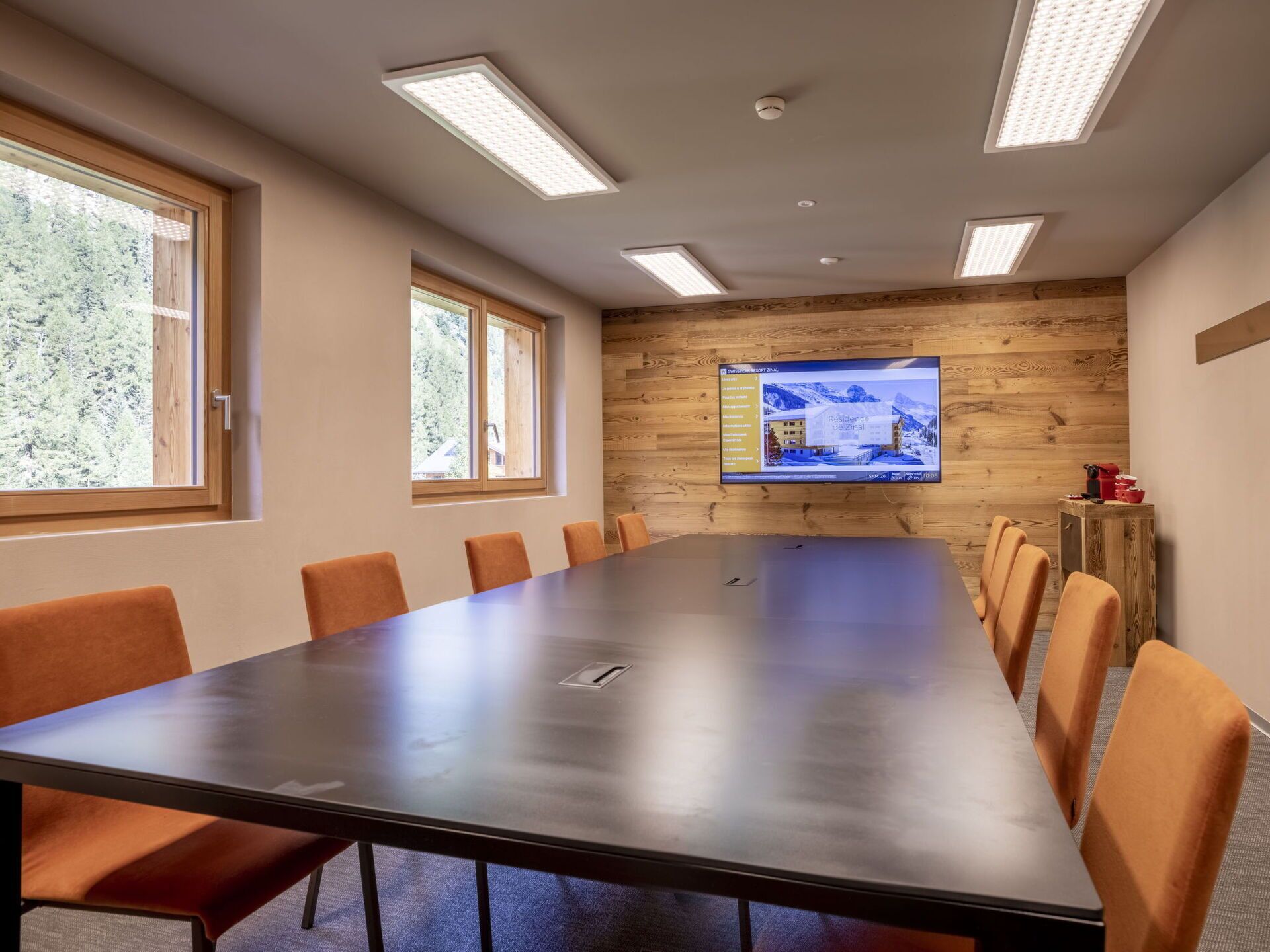A conference room with a long table, six chairs, and a large screen displaying a property image.