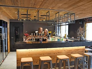 Zona de bar con techo de madera, taburetes y mostrador con grifos.
