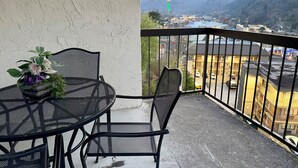Een balkon met een tafel en stoelen, een bloempot en uitzicht op een stad met bergen op de achtergrond.