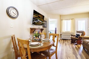 Ein Essbereich mit einem Holztisch, Stühlen, einer Uhr und einem an der Wand befestigten Fernseher.