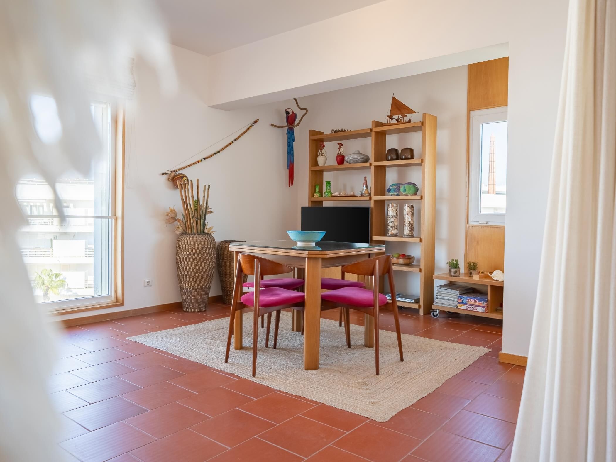 A room with a dining table, chairs, a TV, a bookshelf, and a window.
