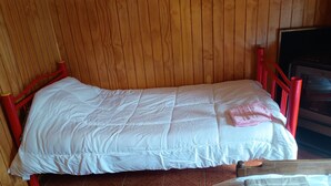 A single bed with a white duvet and a pink towel, wooden panel walls, and a red metal frame.