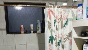 A bathroom with a toilet, a shower curtain with a leaf pattern, and a shelf with toiletries.