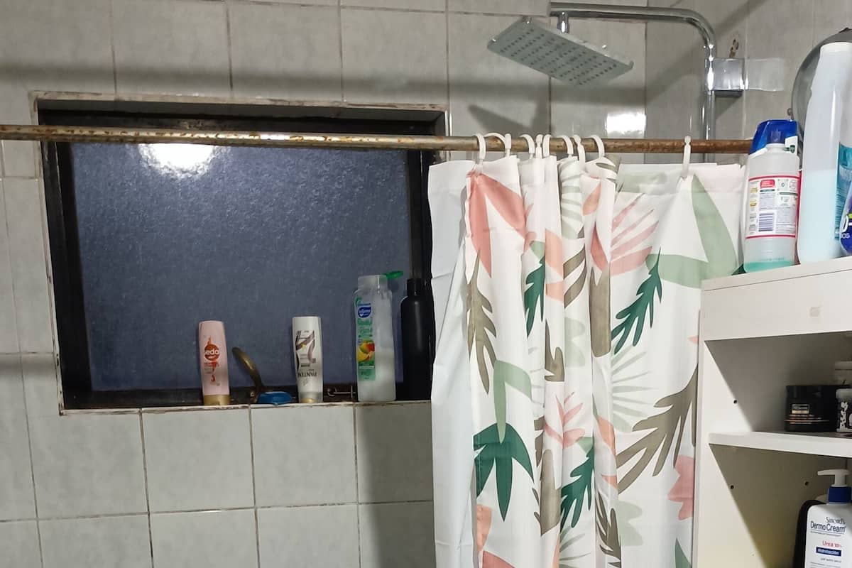 Un baño con inodoro, cortina de ducha con estampado de hojas y estante con artículos de aseo.
