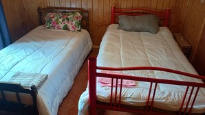 Two single beds with wooden headboards, a nightstand with a lamp, and a wooden wall.