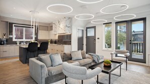Ein modernes Wohnzimmer mit einer Couch, Sesseln, einem Couchtisch und einer Küchenzeile mit Esstisch und Stühlen.