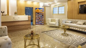 Un hall de hotel con mostrador de recepción, asientos cómodos, un revestimiento decorativo y un cartel.