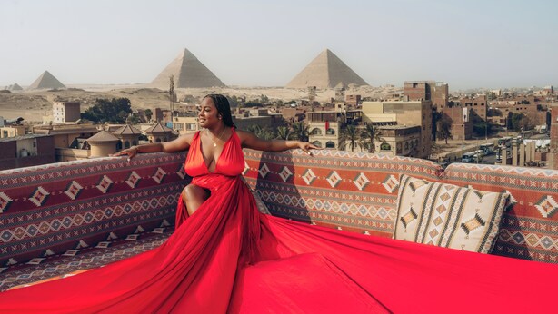Una persona con un vestido rojo sentada en un sofá estampado con vistas a las pirámides.