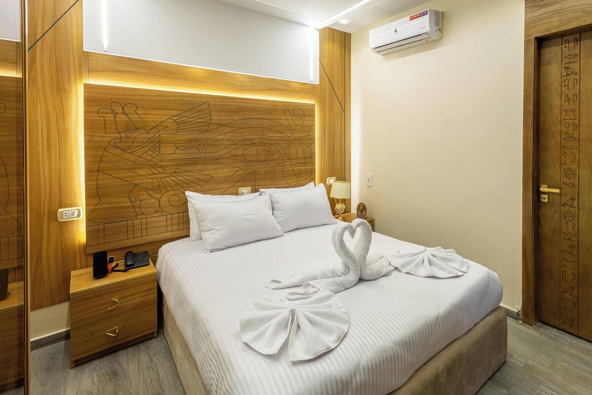 Ein Hotelzimmer mit einem Bett, einem Nachttisch, einem Telefon, einer Wand-Klimaanlage und einer Holztür.