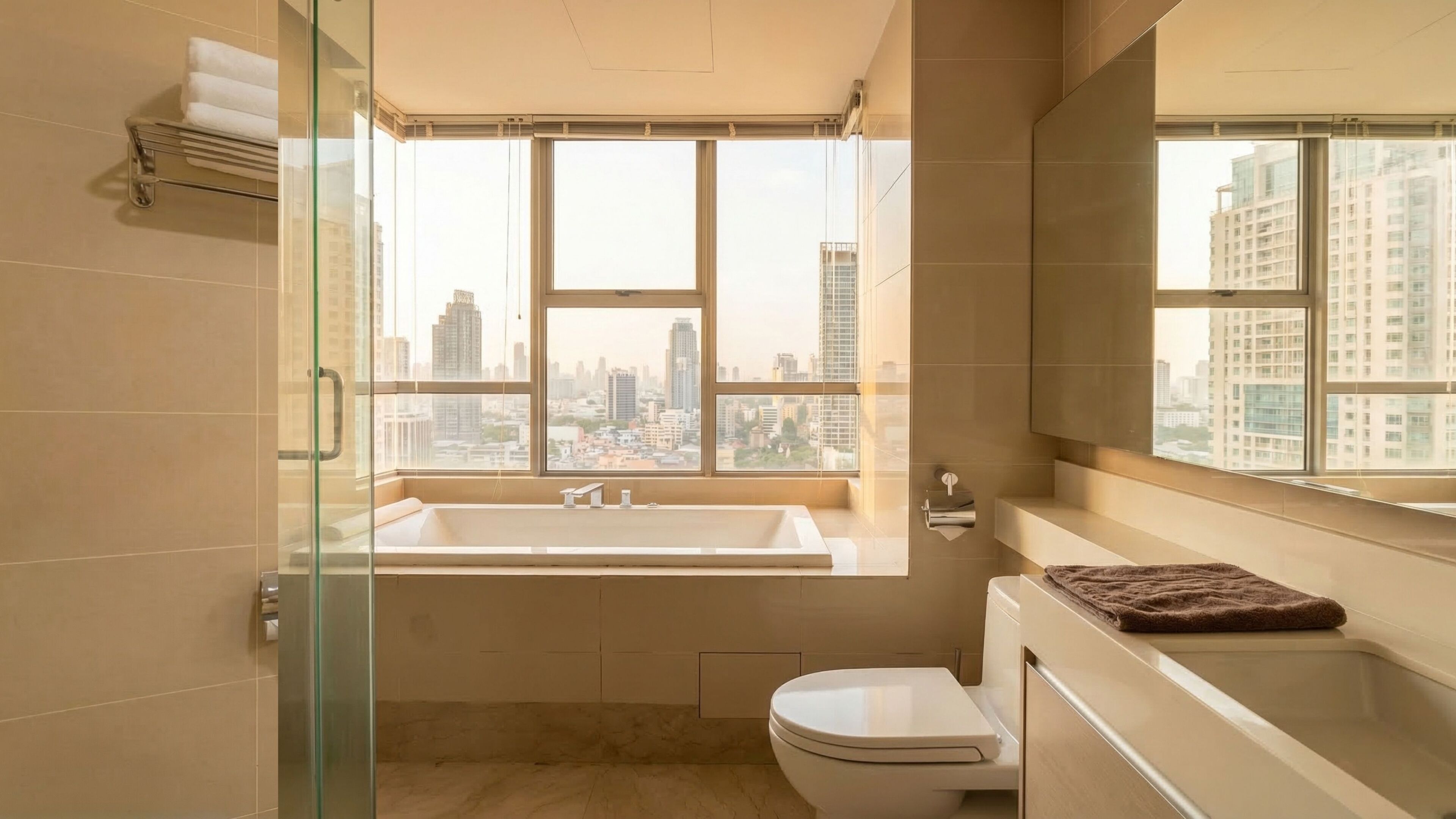 A modern bathroom with a bathtub, toilet, and a large window offering a city view.