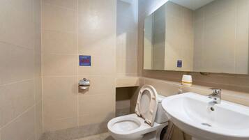 A bathroom with a toilet, sink, and mirror. There are signs on the wall, and a trash bin is visible.