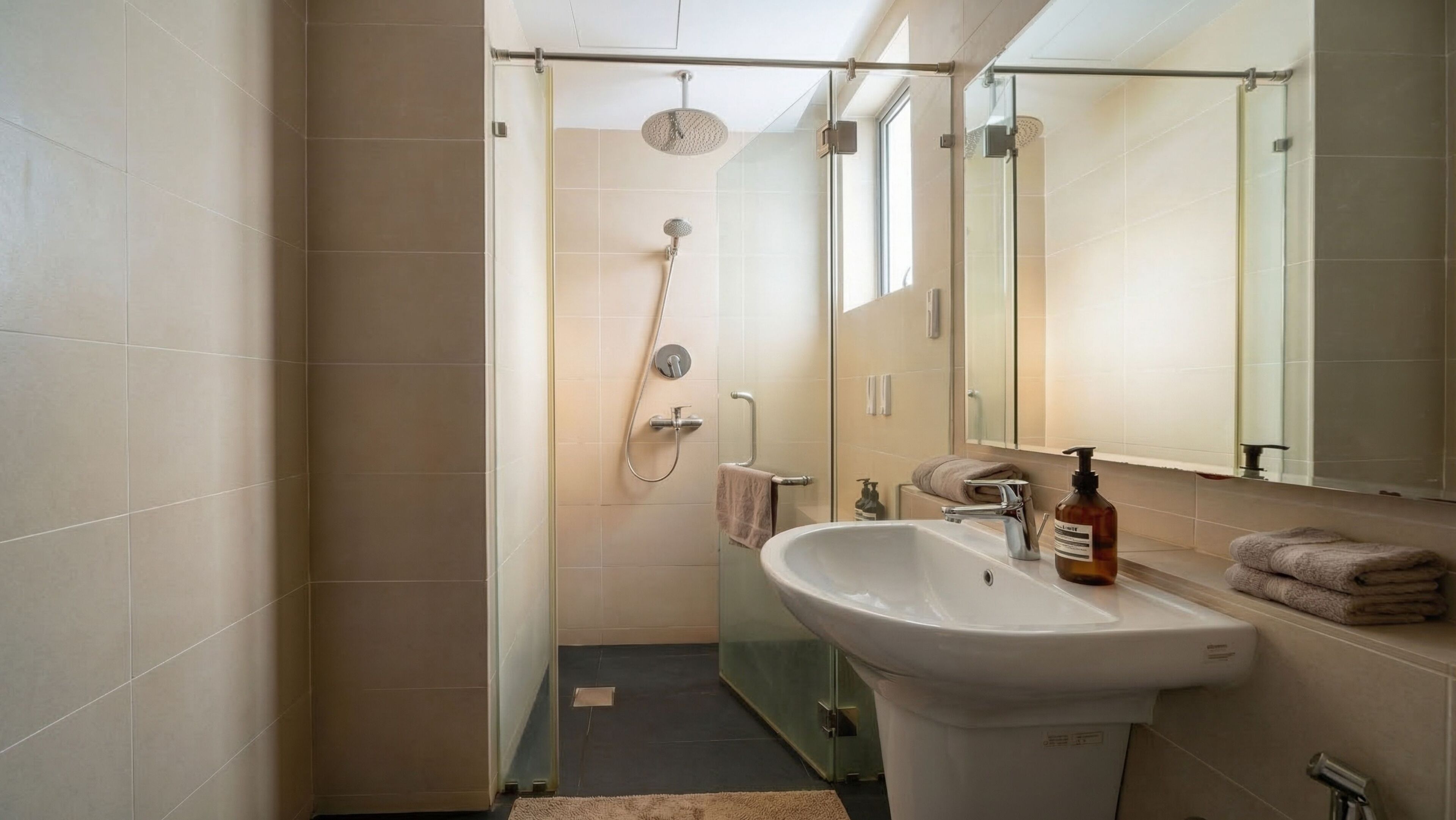 Une salle de bain avec une douche en verre, un lavabo avec un miroir et un flacon de savon.