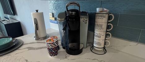 Eine Küchenarbeitsplatte mit Kaffeemaschine, einer Stapel Tassen und einem Mülleimer.